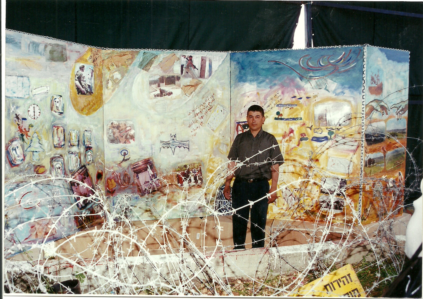 الكاتب الدكتور يوسف غزاوي أمام جدارية الزنزانة - ملتقى الخيام 2001