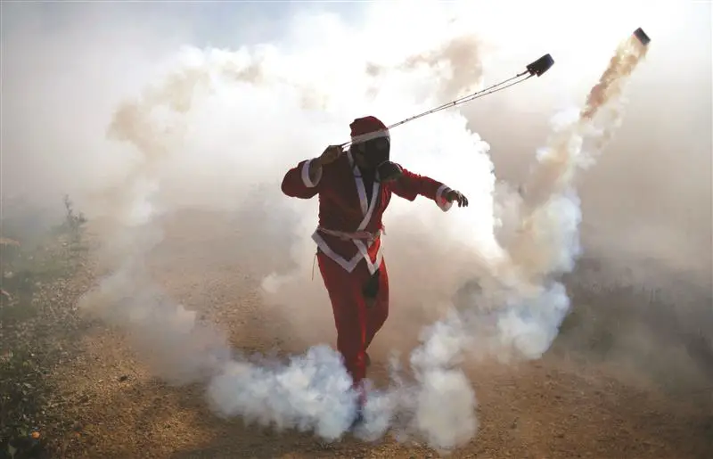 فلسطيني يرتدي زي «سانتا كلوس» خلال مواجهات مع جنود الاحتلال ضد الاستيطان في الضفة الغربية أمس (رويترز)