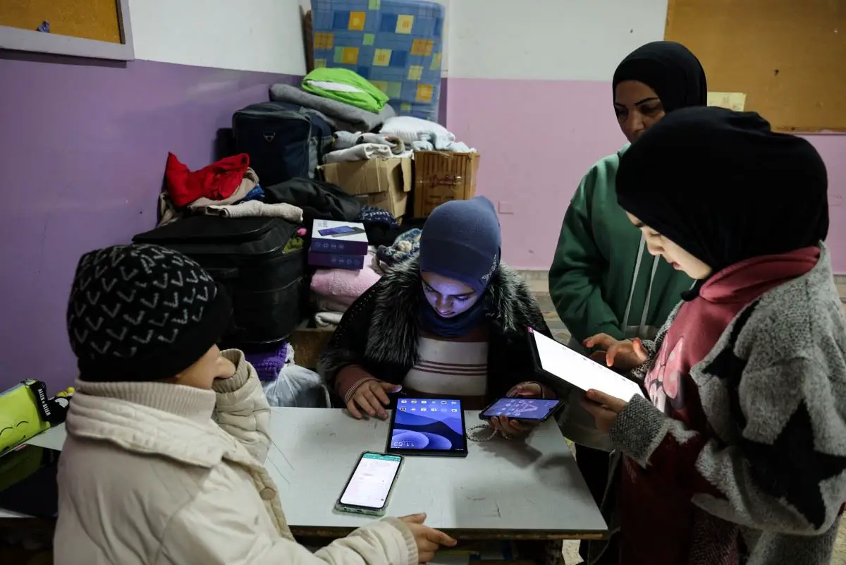 طلاب نازحون في إحدى مراكز الإيواء في مدارس صور يتابعون دروسهم عبر الأجهزة الالكترونية (أف  ب)
