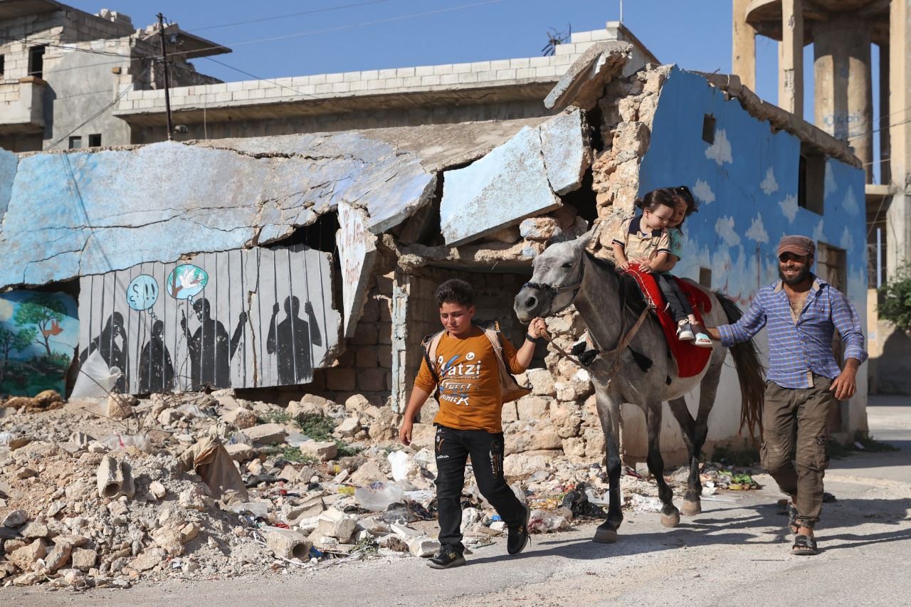 أطفال على حصان يمرون أمام مبنى مدمر في بلدة بنش في محافظة إدلب شمال غرب سوريا (9 تموز 2022، أ ف ب).